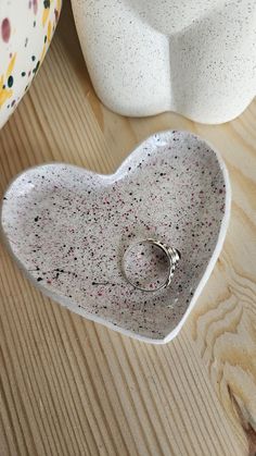 a white heart shaped dish with a ring on it sitting next to a ceramic vase