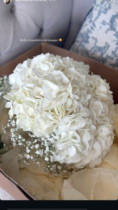 a bouquet of white flowers sitting in a box on a couch with pillows behind it