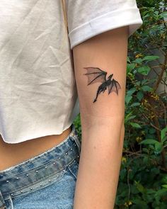 a woman's arm with a small black bat tattoo on the left inner arm