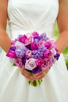 a bride holding a bouquet of purple and pink flowers