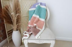 a chair with a blanket on it next to a potted plant and a white vase