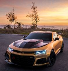 a gold chevrolet camaro with black stripes on it's hood is parked in a parking lot