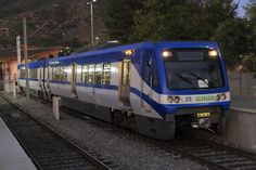 a blue and white train traveling down tracks next to a station at night with mountains in the background