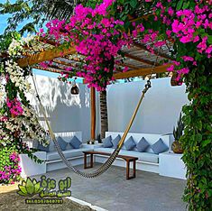 an outdoor seating area with pink flowers and greenery on the roof, along with a hammock