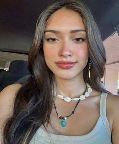 a woman with long brown hair wearing a white top and blue beads on her necklace