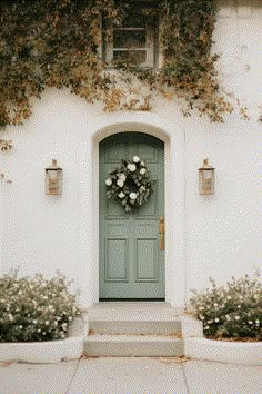 a green door and two planters with white flowers on the side of a house