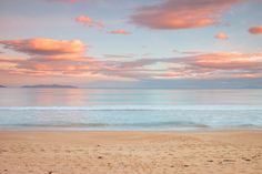 an ocean view with pink clouds in the sky and some blue water on the beach