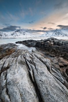 the rocks are covered with snow and ice as the sun sets over mountains in the distance