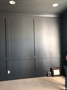 a man standing in front of a black paneled wall and framed photograph on the floor