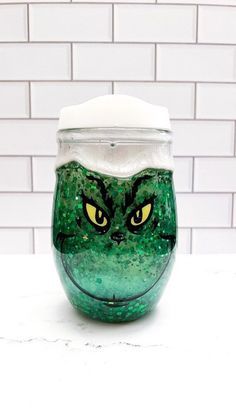 a green glass cup with yellow eyes and a white top on a table next to a brick wall