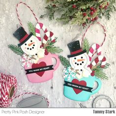 two snowmen in mugs hanging from the side of a christmas ornament