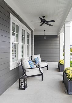 a porch with two chairs and a fan on the ceiling, along with flowers in planters