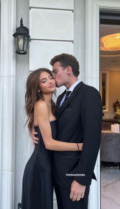 a man in a suit kissing a woman in a black dress on the steps of a building