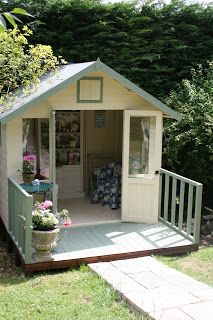 a small garden shed in the middle of a yard with flowers and potted plants