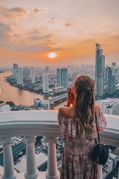 a woman standing on top of a tall building looking at the cityscape and water