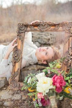 a woman laying down in front of a mirror with flowers on the ground next to it