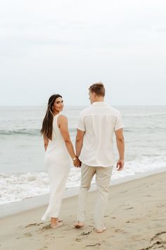 a man and woman walking on the beach holding hands