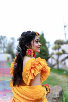 a woman in an orange dress with flowers on her head and long hair standing outside