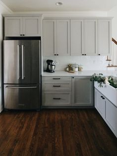 a stainless steel refrigerator in a white kitchen with wood flooring and wooden stairs leading up to the upper level