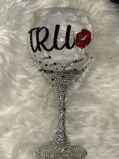 a wine glass with the word true painted on it sitting on a white fur covered surface