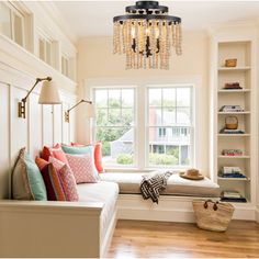 a room with a window seat, bookshelf and a chandelier hanging from the ceiling