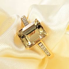 a fancy ring with an emerald and diamond set in yellow gold on a white satin background