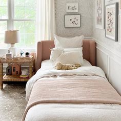 a small bed with pillows and blankets in a room next to a window that has pictures on the wall