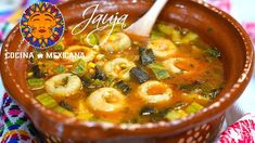 a brown bowl filled with soup and shrimp on top of a colorful table cloth next to a wooden spoon