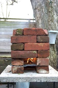 a brick oven sitting on top of a cement block structure in front of a tree