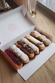 an open box filled with different types of doughnuts on top of a wooden table