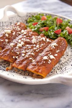 two enchiladas are sitting on a plate next to a side of salad