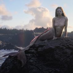 a woman sitting on top of a rock next to a body of water