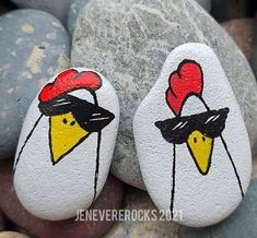 two painted rocks with roosters on them are sitting next to some rocks and pebbles