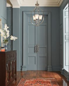 a hallway with blue walls and wooden floors, an ornate chandelier hangs from the ceiling