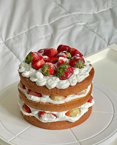 a three layer cake with strawberries and whipped cream on top is sitting on a white plate