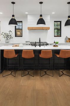 a kitchen with black and white cabinets, wood floors, and pendant lights over the island