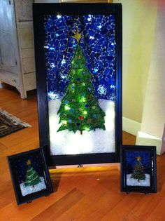 a christmas tree is displayed in front of two small frames with lights on the bottom