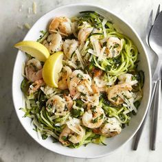 a white bowl filled with shrimp and zucchini noodles next to a lemon wedge