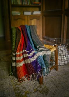 a multicolored blanket sitting on top of a wooden chair next to a basket