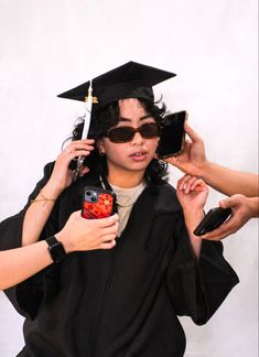 a woman is getting her graduation cap and gown put on by two other women holding cell phones