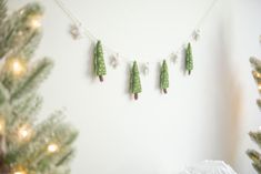 christmas decorations hanging on the wall in front of a white wall with green trees and lights