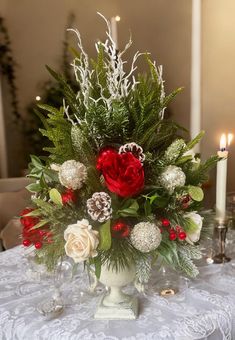 a white vase filled with flowers and greenery on top of a table next to candles