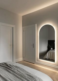 a bedroom with white walls and lights on the mirror above the bed, along with two doors leading to another room