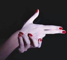 a woman's hand with red nail polish holding something in her left hand, against a black background