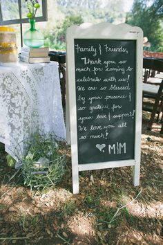 a chalkboard sign sitting on top of a grass covered field next to a table