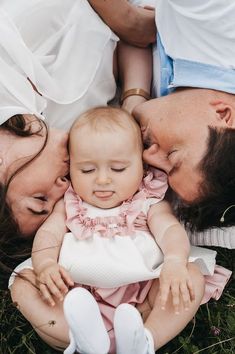 two adults and a baby laying on the grass together with their heads touching each other