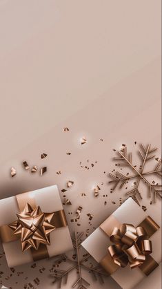 two gift boxes with gold bows and snowflakes on the top are surrounded by confetti