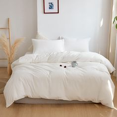 an unmade bed with white sheets and pillows on the floor next to a potted plant