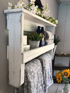 a white shelf filled with towels and flowers on top of a table next to a potted plant