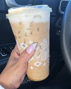 a woman holding a cup of coffee in her hand while sitting in the drivers seat of a car